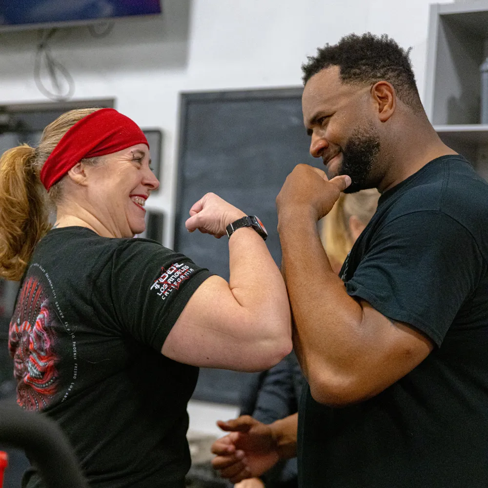 Two True Grit Fitness members flexing and smiling together after a workout