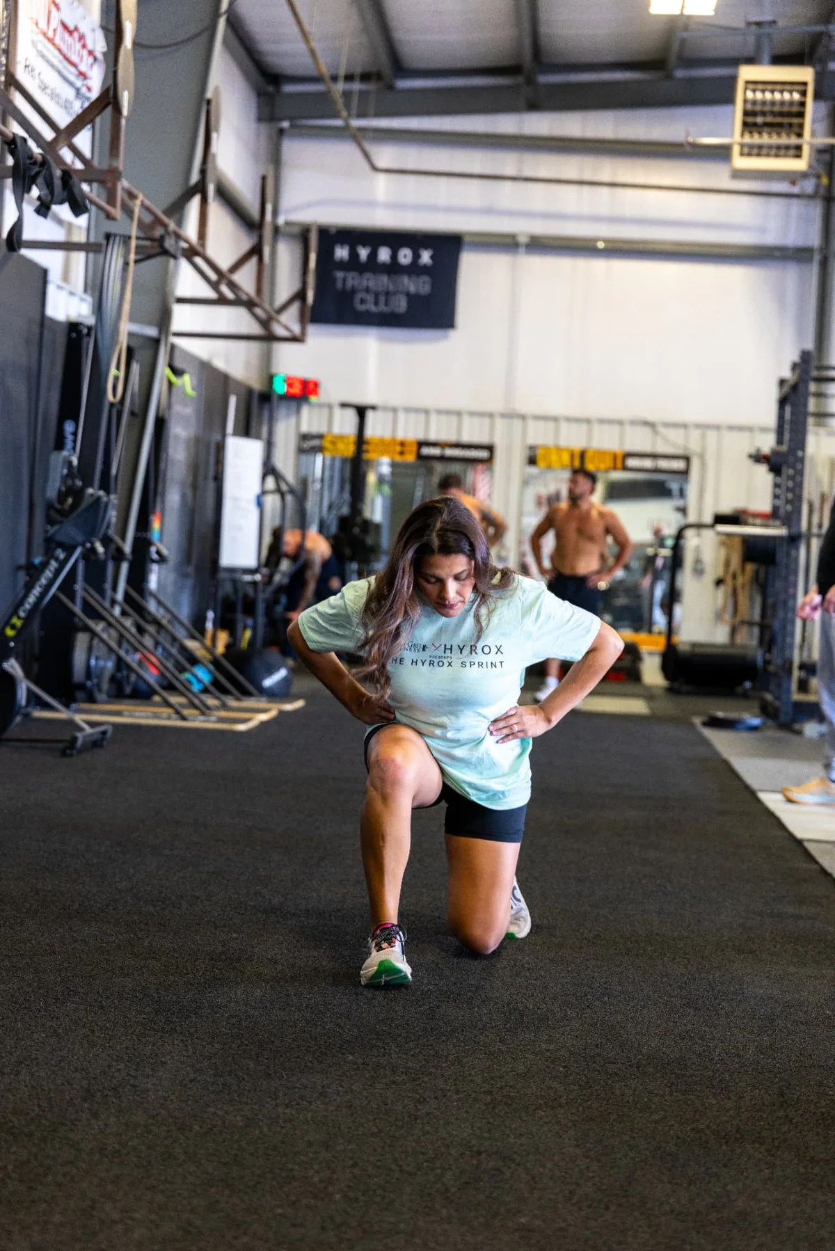 Laura Billiot training in a HYROX Sprint shirt on the floor at True Grit Fitness, a HYROX affiliate gym in Edmond, Oklahoma