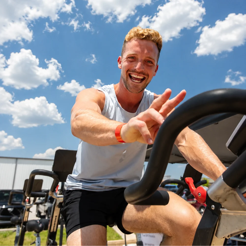 Smiling athlete on an assault bike during an outdoor True Grit Fitness workout in Edmond, Oklahoma