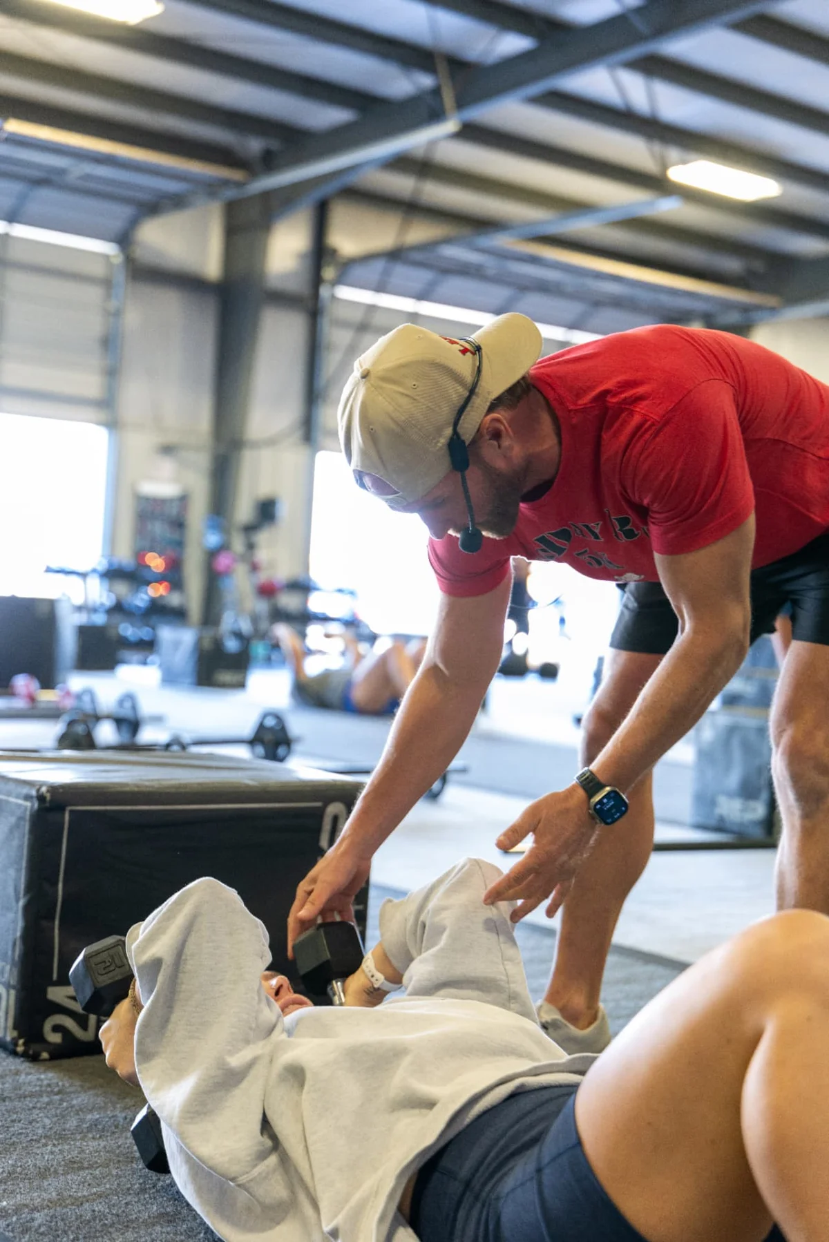 Travis Grimm coaching a member through a dumbbell press on the gym floor at True Grit Fitness in Edmond, Oklahoma