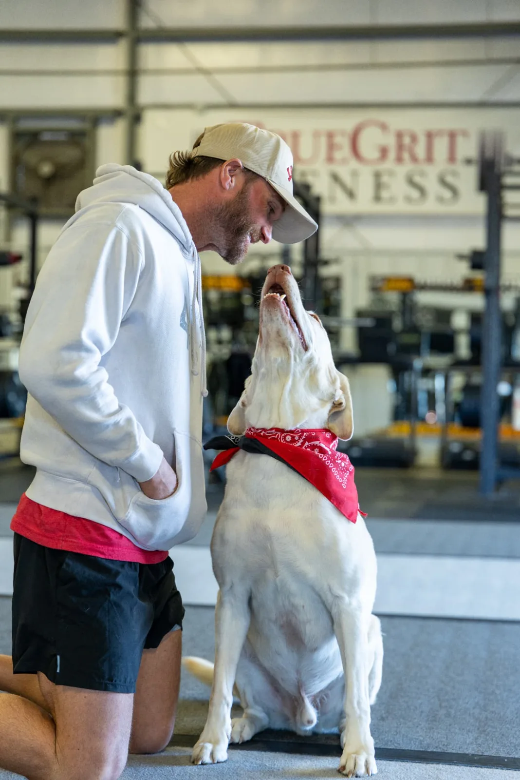 Travis Grimm kneeling with Charlie the gym dog on the training floor at True Grit Fitness