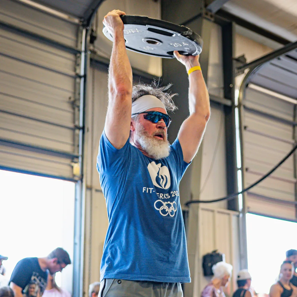 Masters athlete pressing a 45 lb plate overhead during a True Grit Fitness Hyrox event