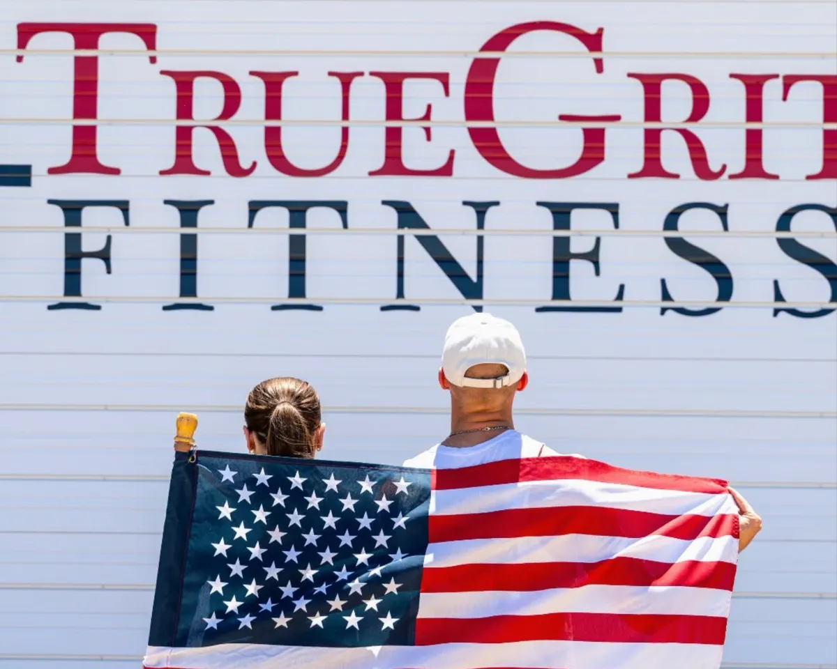 Two members holding an American flag in front of the True Grit Fitness sign in Edmond, Oklahoma